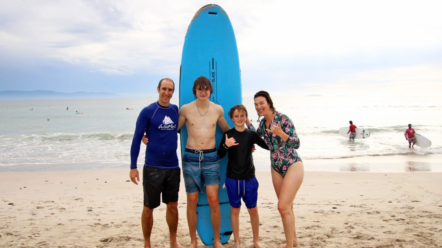 Happy family hugging after surf lesson at La Lancha beach in Punta Mita