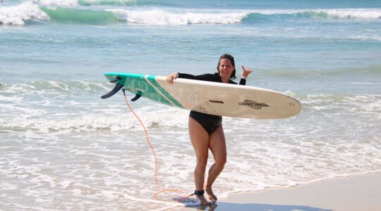 Happy surfer walking out of the ocean with a board after a lesson at La Lancha