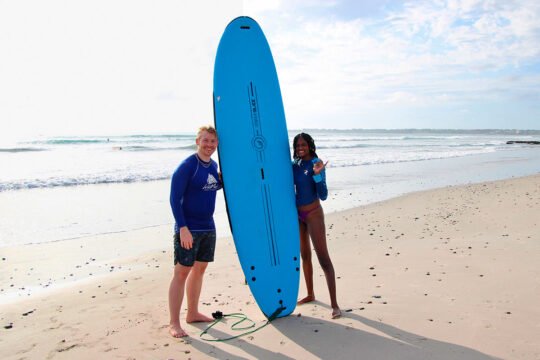 Two friends smiling with a surfboard after a lesson at La Lancha beach