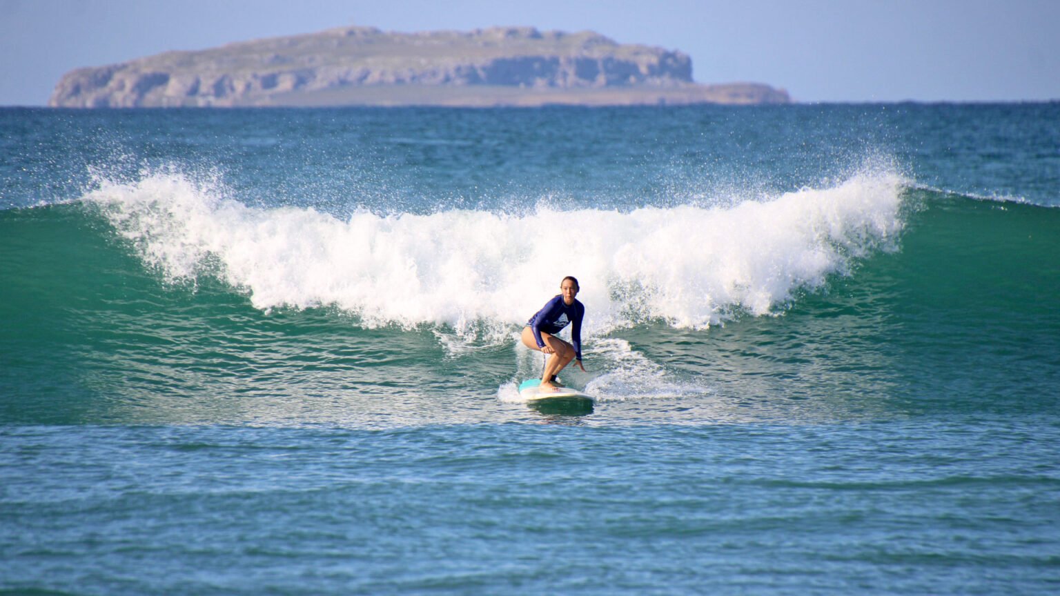 Female surfer riding a wave with foam trail and Marietas Islands in the background at Punta Mita
