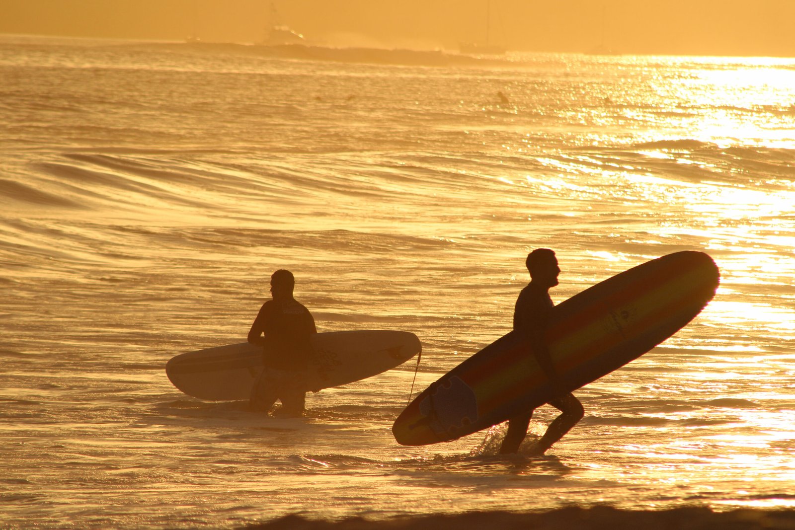 Golden hour sunset light illuminating the beach as two surfers exit the water at La Lancha, Nayarit.