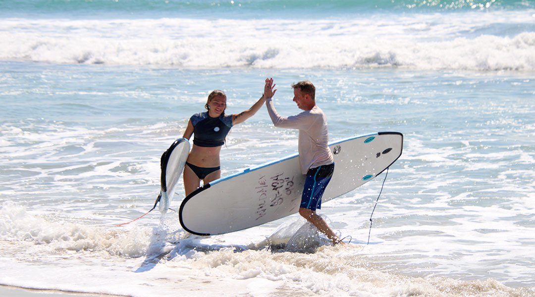 LTwo surfers giving a high five while walking out of the ocean with soft-top surfboards at La Lancha